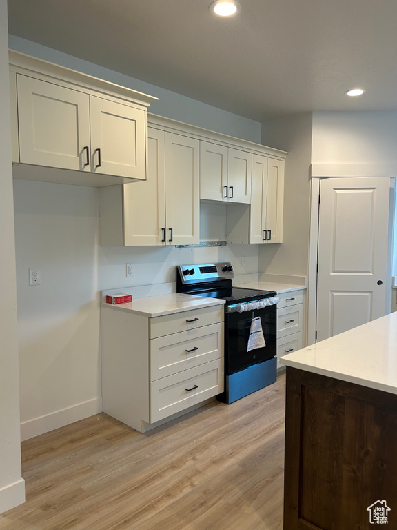 Kitchen with stainless steel electric stove, light wood-style floors, recessed lighting, light countertops, and white cabinetry