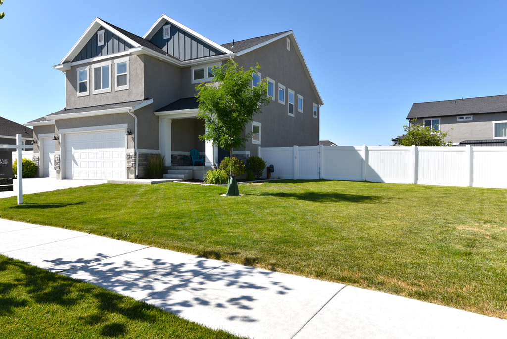 View of front of home with a garage, stucco siding, board and batten siding, stone siding, and driveway