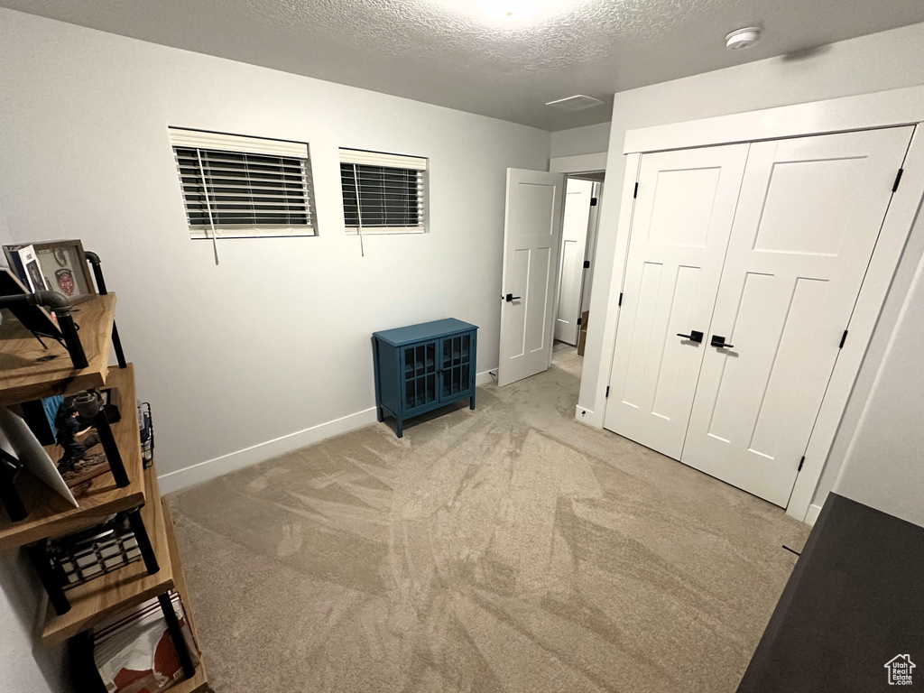 Unfurnished bedroom featuring a textured ceiling, baseboards, light carpet, and a closet