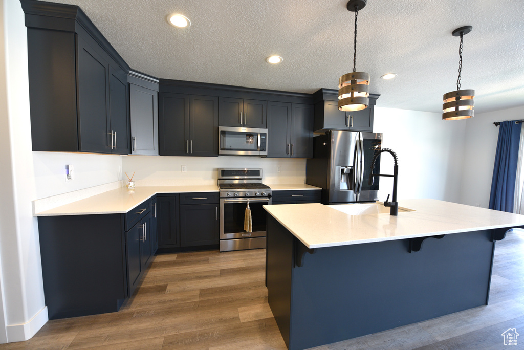 Kitchen with stainless steel appliances, a breakfast bar area, light countertops, wood finished floors, and a textured ceiling