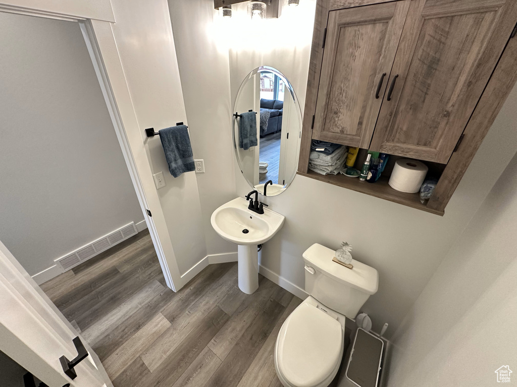 Half bath featuring wood finished floors, baseboards, toilet, and a sink
