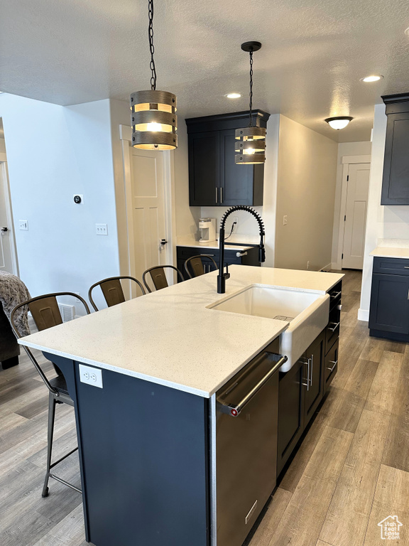 Kitchen featuring dishwasher, a sink, a kitchen breakfast bar, light wood finished floors, and a textured ceiling