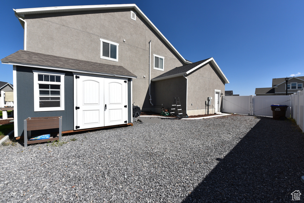 Back of house with a gate, stucco siding, and a storage unit