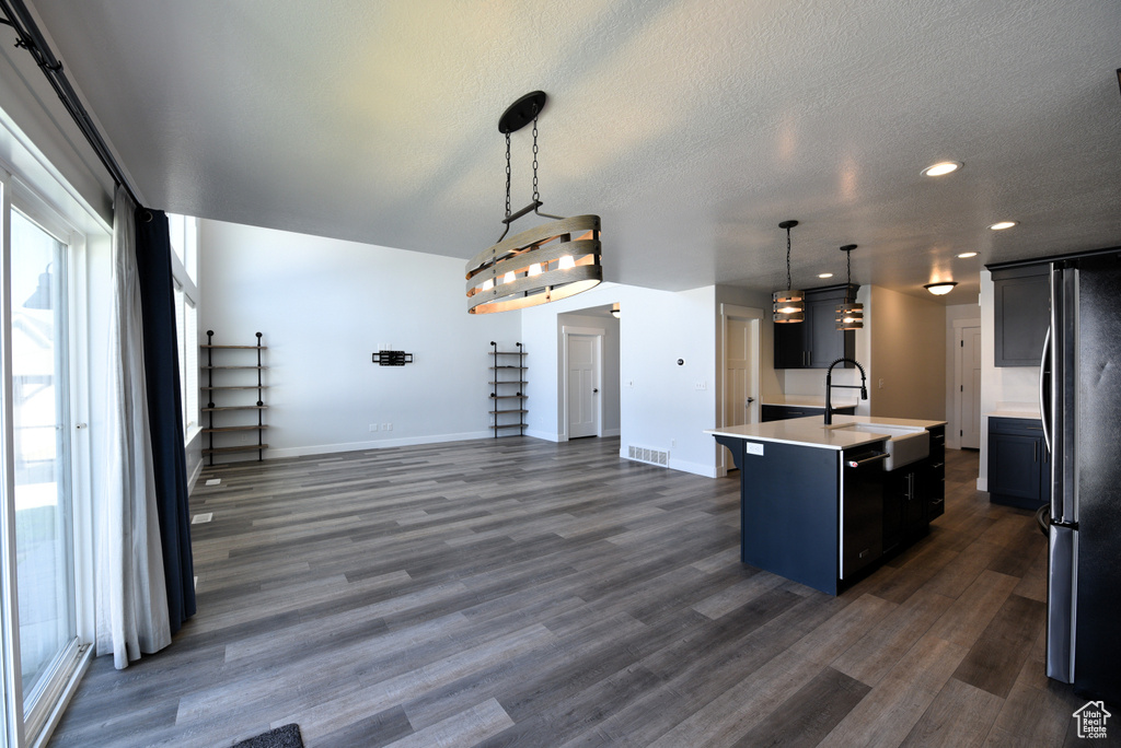 Kitchen with freestanding refrigerator, light countertops, a kitchen island with sink, dark wood-style floors, and dishwashing machine