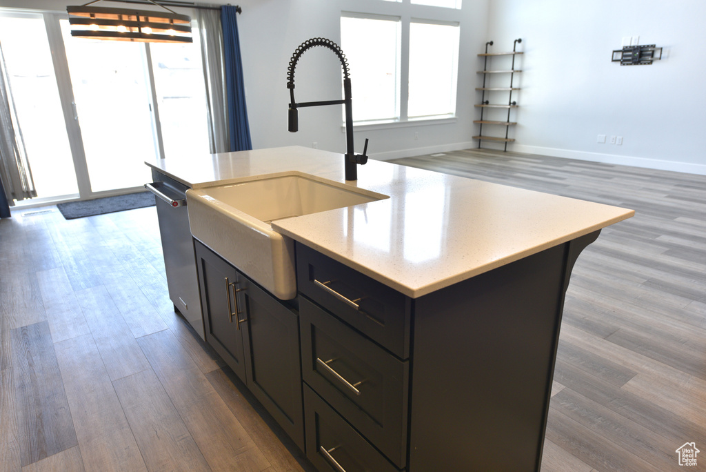Kitchen with wood finished floors, stainless steel dishwasher, a center island with sink, light stone countertops, and open floor plan