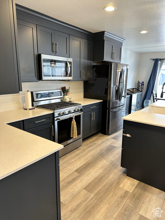 Kitchen featuring stainless steel appliances, a textured ceiling, light wood-style floors, a sink, and recessed lighting