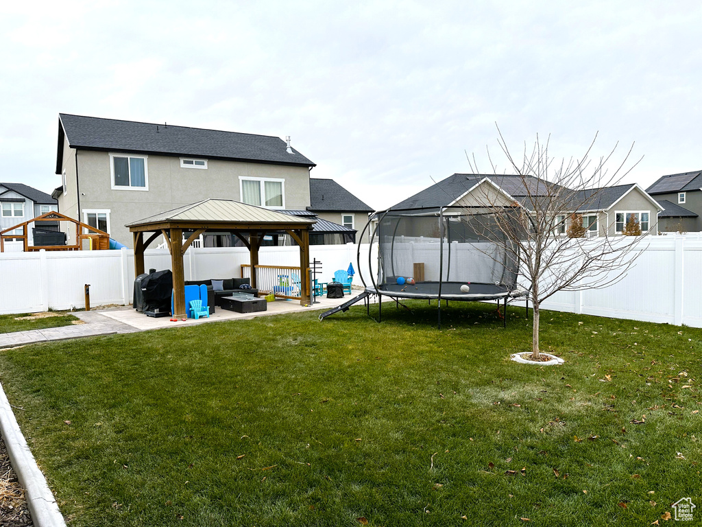 Rear view of property with a gazebo, a trampoline, a patio area, a fire pit, and stucco siding