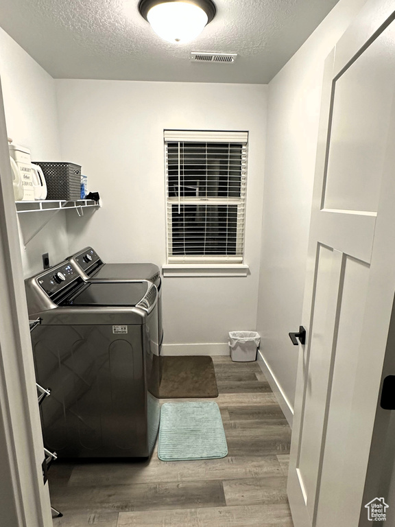 Washroom featuring washing machine and clothes dryer, a textured ceiling, wood finished floors, and baseboards