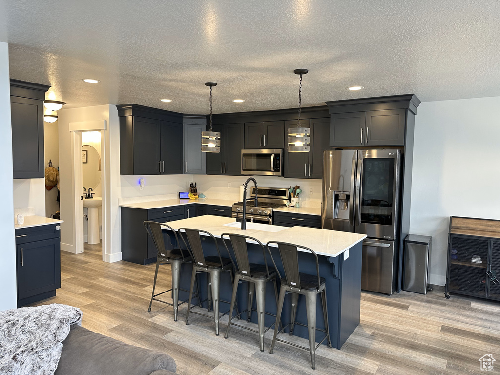 Kitchen featuring stainless steel appliances, light wood-type flooring, a textured ceiling, a kitchen bar, and light countertops