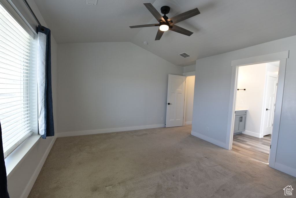 Unfurnished bedroom featuring light carpet, vaulted ceiling, a ceiling fan, and ensuite bath