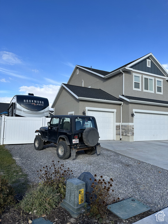 View of side of property with concrete driveway, fence, stucco siding, board and batten siding, and stone siding
