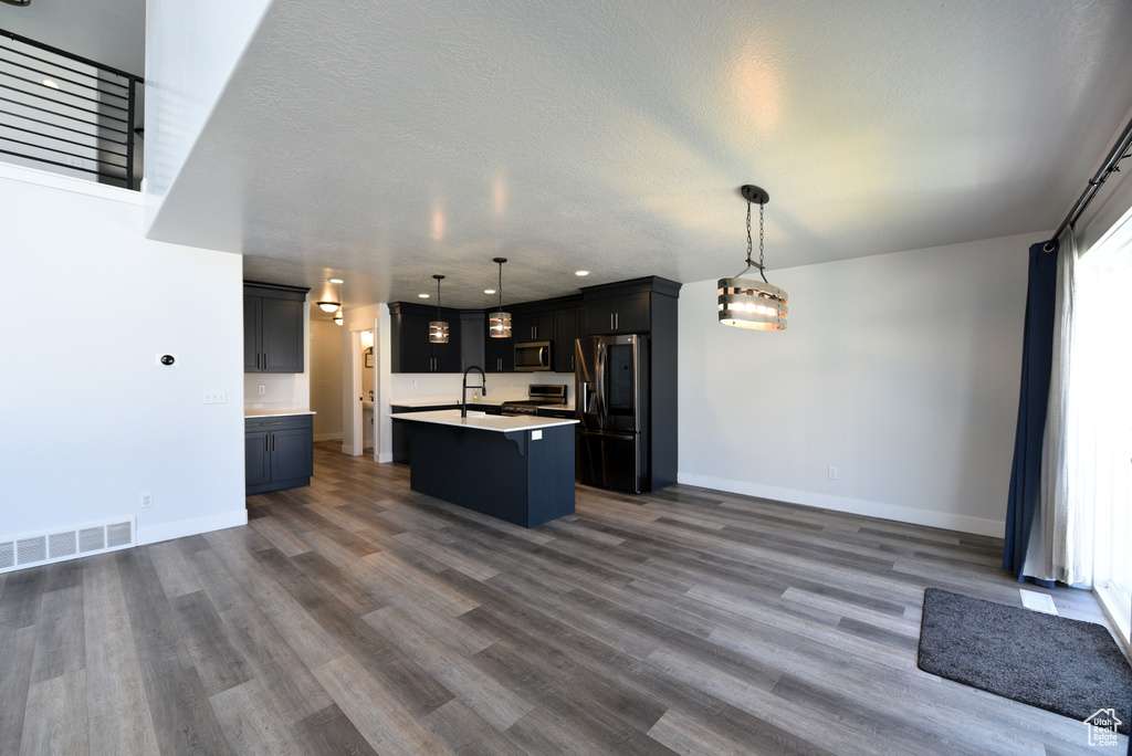 Kitchen with appliances with stainless steel finishes, open floor plan, a center island with sink, dark wood-style flooring, and a textured ceiling
