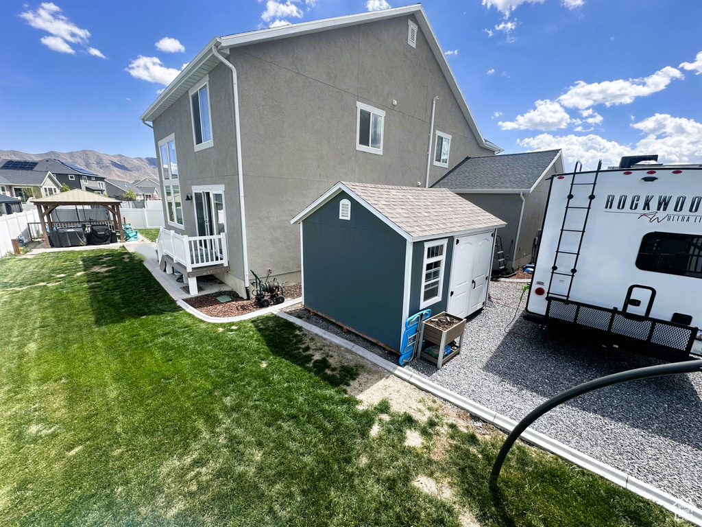 Rear view of house featuring a lawn, an outdoor structure, stucco siding, a gazebo, and a shed