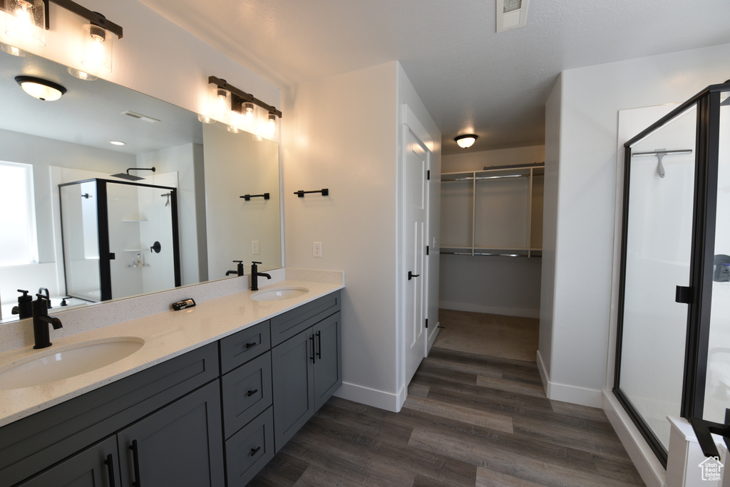 Bathroom with double vanity, a shower stall, wood finished floors, and a walk in closet