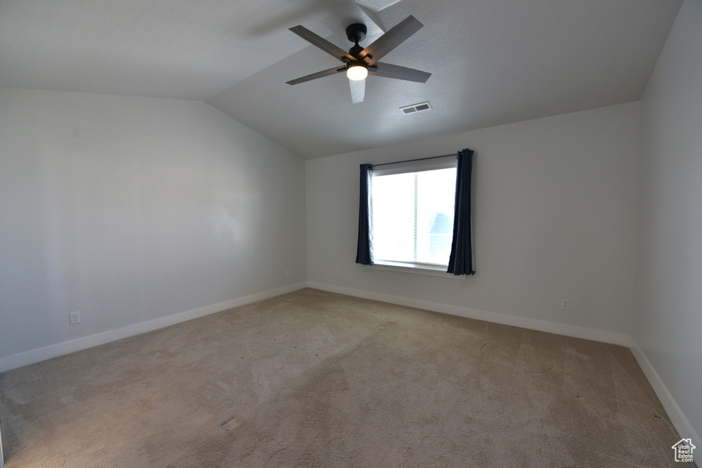 Empty room with light colored carpet, vaulted ceiling, and a ceiling fan