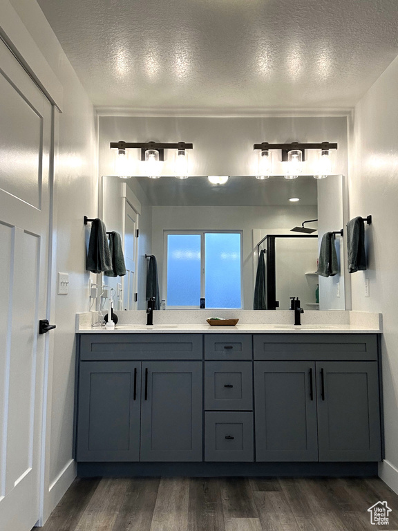 Full bath with a textured ceiling, wood finished floors, a stall shower, double vanity, and baseboards