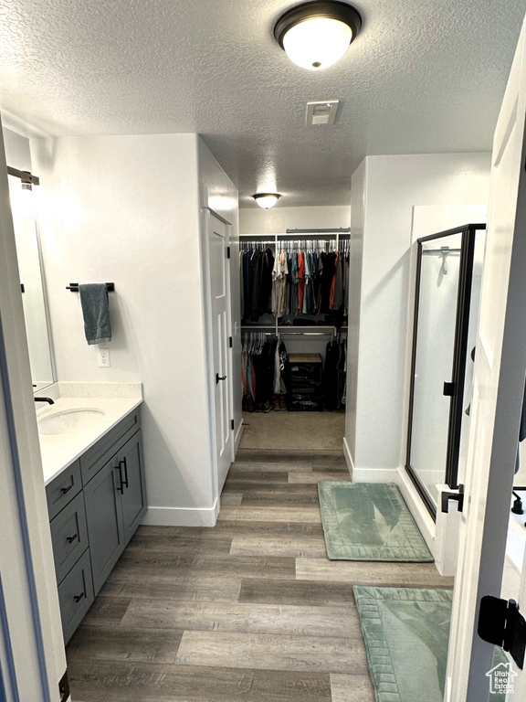 Full bathroom with a textured ceiling, wood finished floors, a stall shower, a spacious closet, and vanity