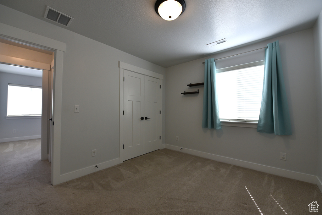 Unfurnished bedroom with light colored carpet, a textured ceiling, and a closet