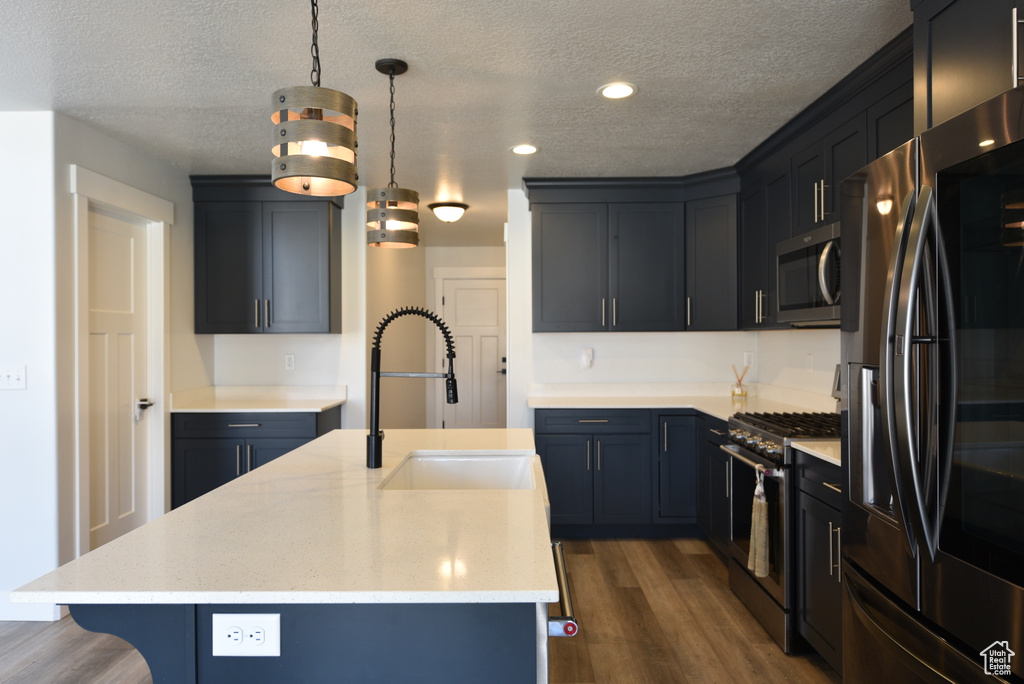Kitchen featuring appliances with stainless steel finishes, dark wood-style floors, a textured ceiling, recessed lighting, and a center island with sink