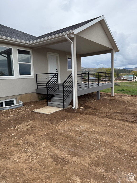 Property entrance with stucco siding, a shingled roof, and a porch