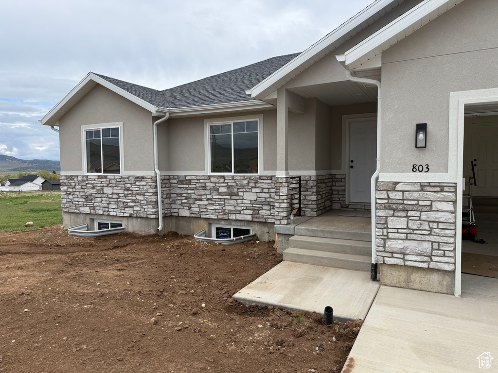 View of exterior entry featuring stone siding, stucco siding, and roof with shingles
