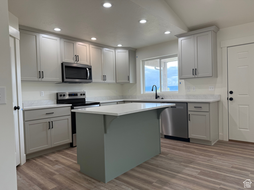 Kitchen with stainless steel appliances, a sink, wood finished floors, a center island, and recessed lighting