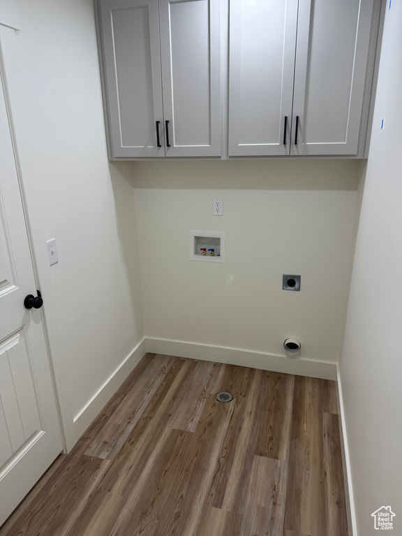 Clothes washing area with electric dryer hookup, hookup for a washing machine, wood finished floors, and cabinet space