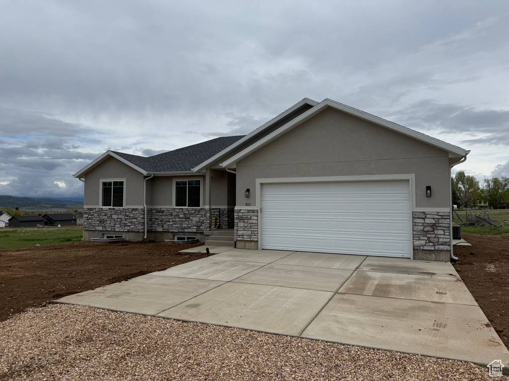 Single story home with stone siding, stucco siding, concrete driveway, and an attached garage