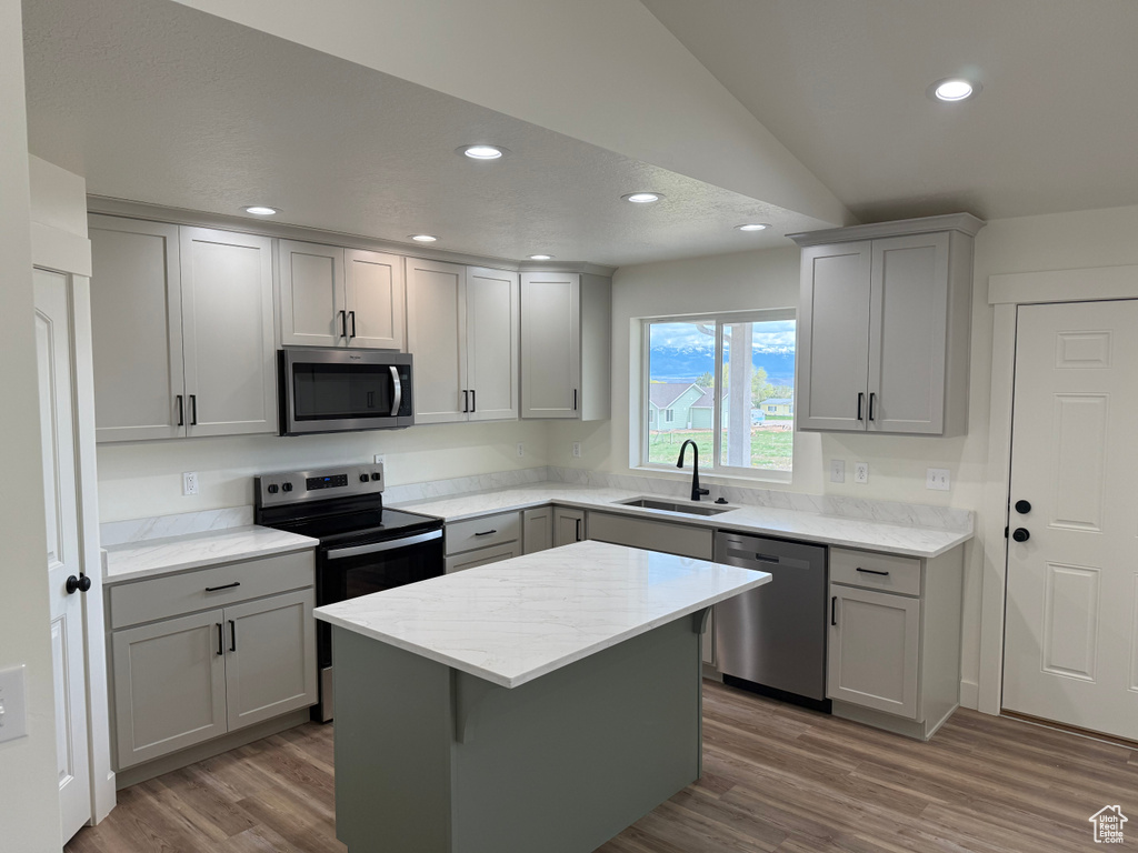 Kitchen with appliances with stainless steel finishes, a sink, gray cabinetry, wood finished floors, and lofted ceiling