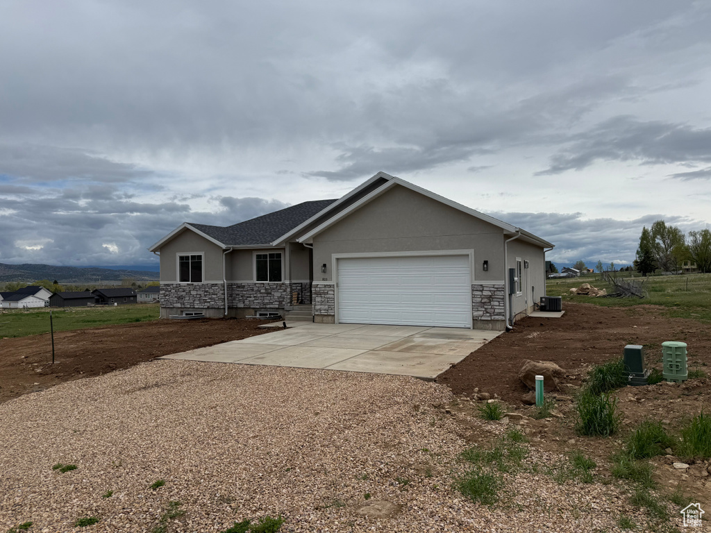 Single story home featuring driveway, an attached garage, stucco siding, central AC, and stone siding