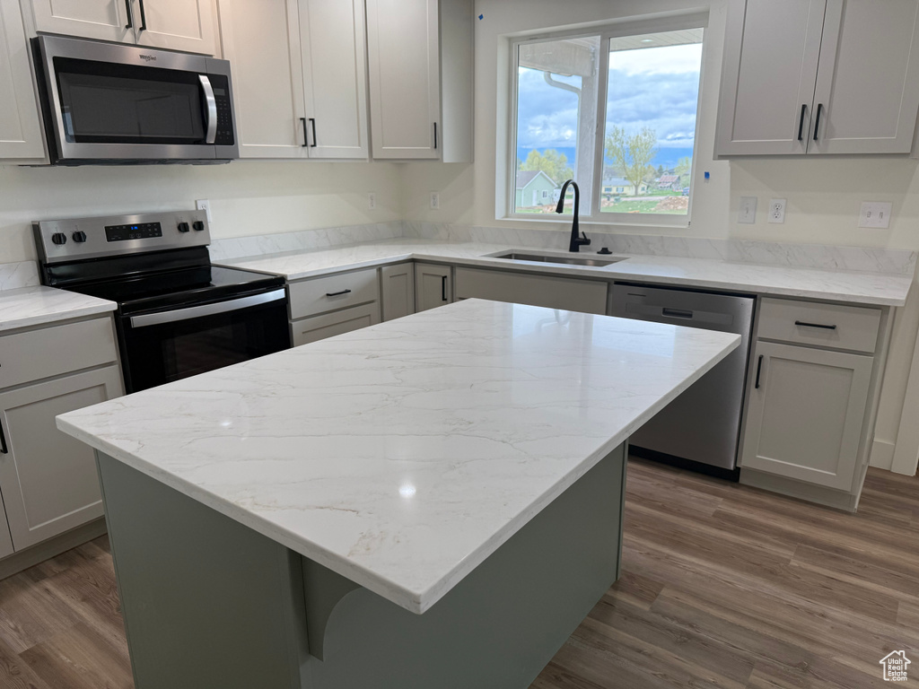 Kitchen with appliances with stainless steel finishes, a sink, wood finished floors, a kitchen island, and light stone counters