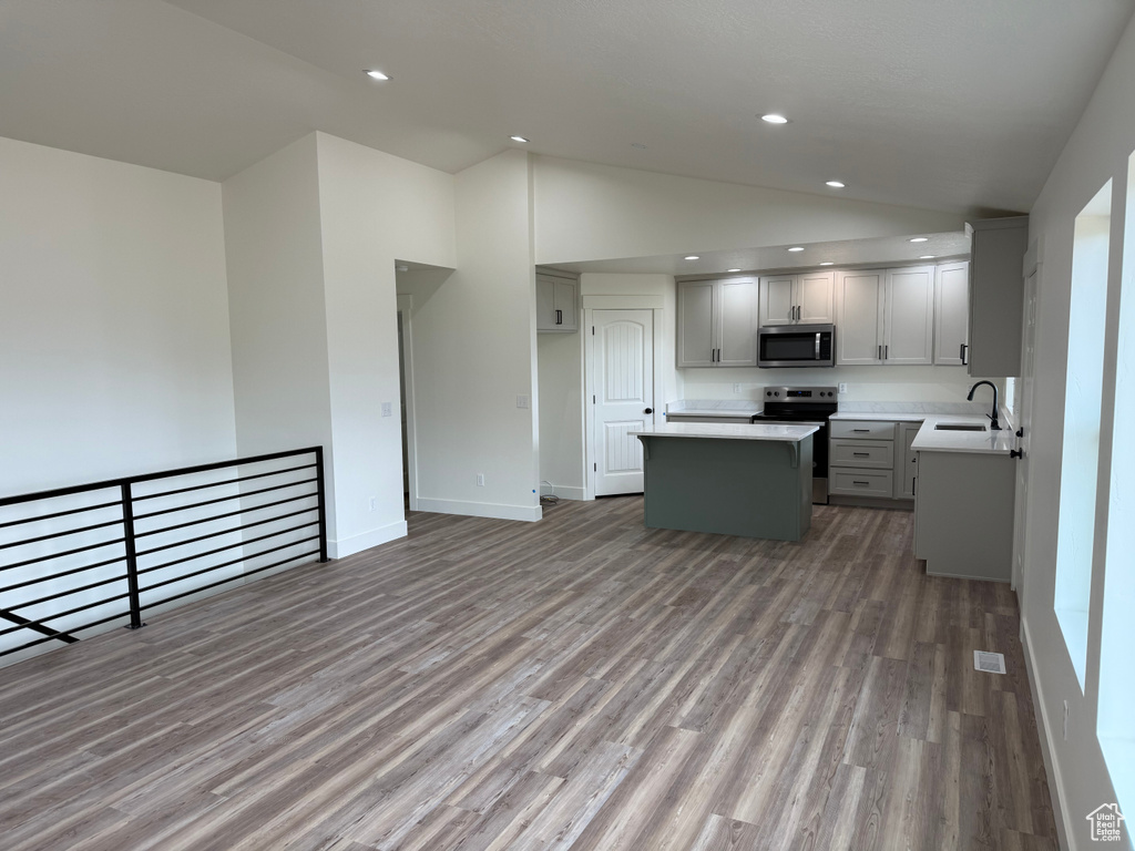 Kitchen with stainless steel appliances, a sink, a center island, vaulted ceiling, and light wood-style floors