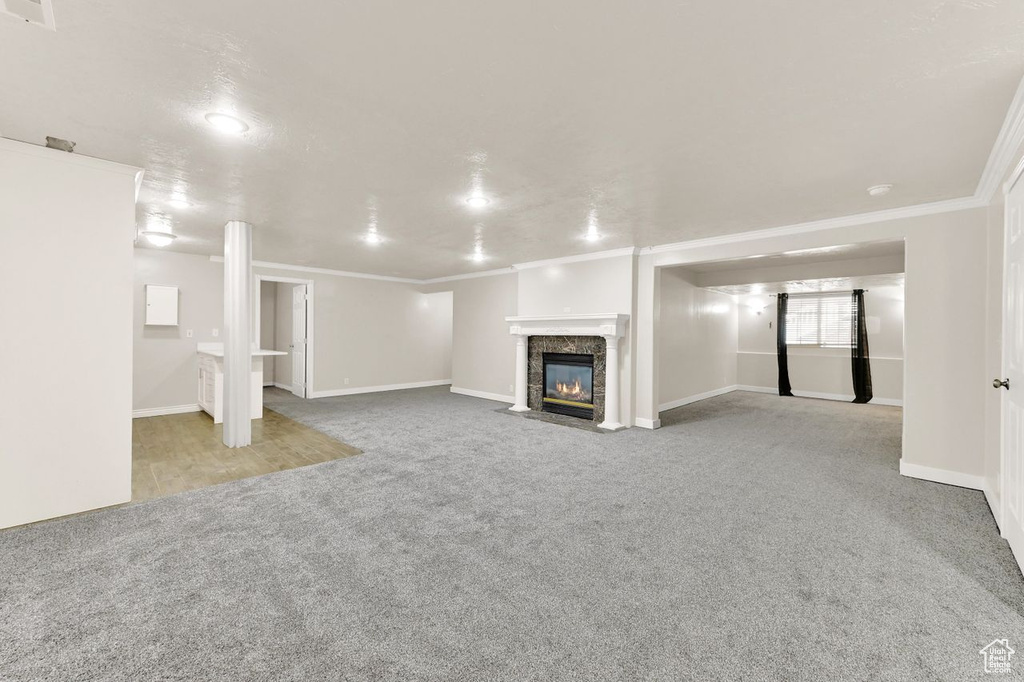 Unfurnished living room featuring carpet floors, a fireplace with flush hearth, ornamental molding, and baseboards