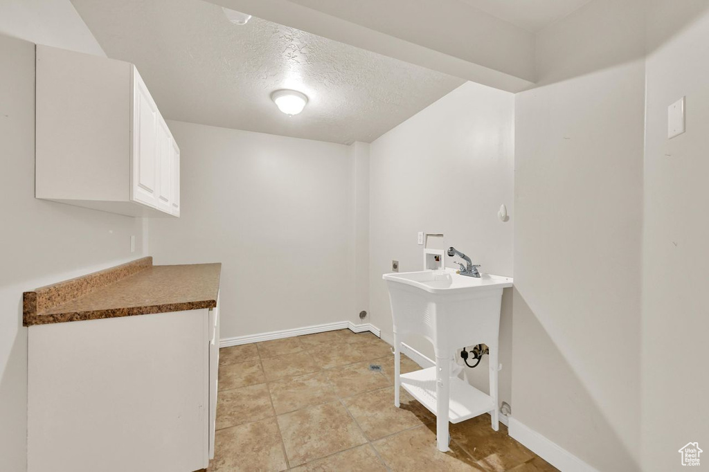 Laundry area with electric dryer hookup, hookup for a washing machine, a textured ceiling, baseboards, and cabinet space