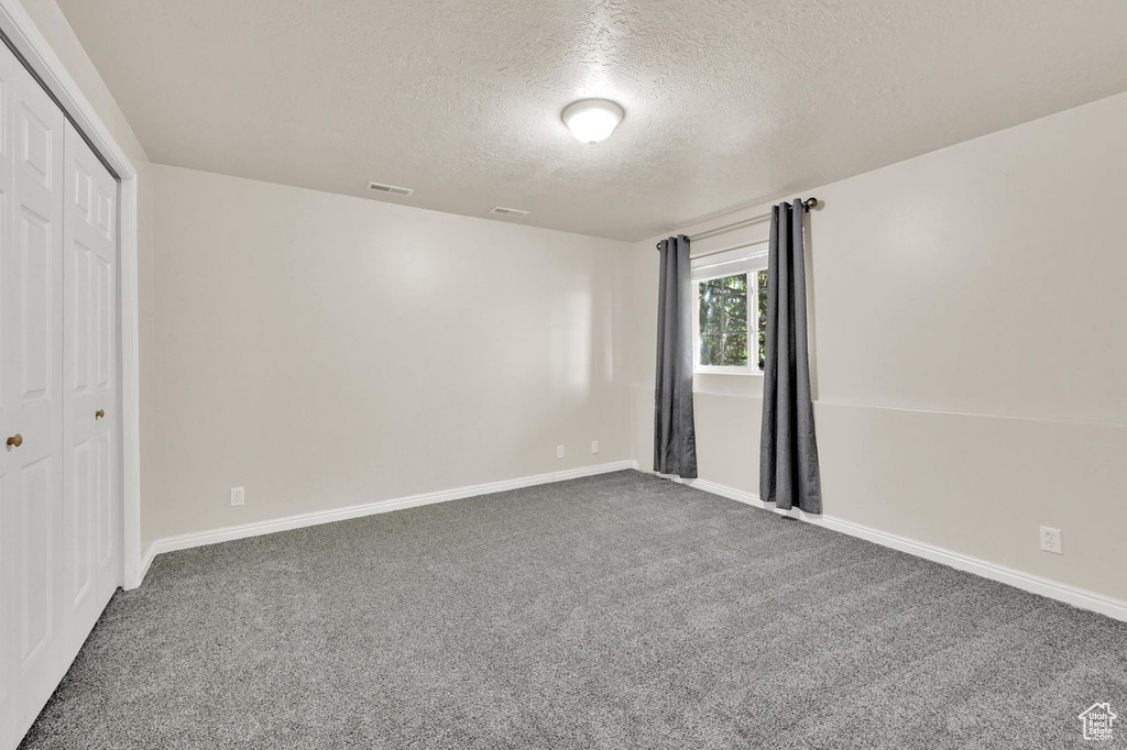 Unfurnished bedroom with a textured ceiling, carpet, a closet, and baseboards