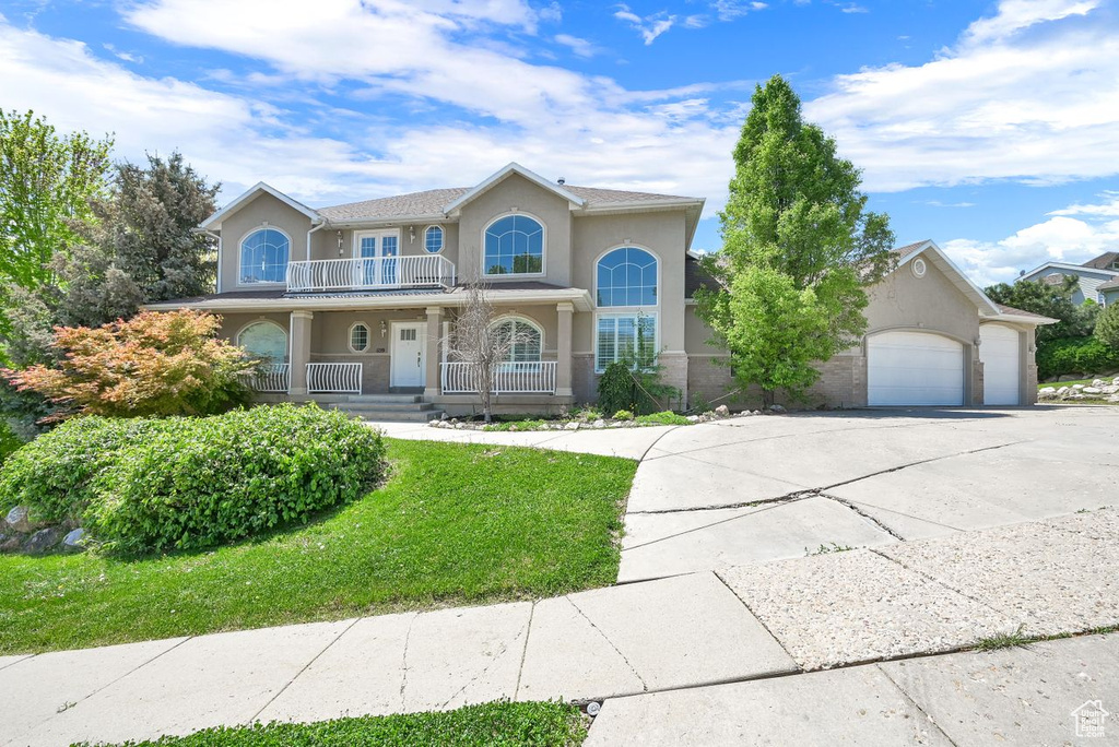 View of front of property featuring a balcony, covered porch, concrete driveway, stucco siding, and an attached garage