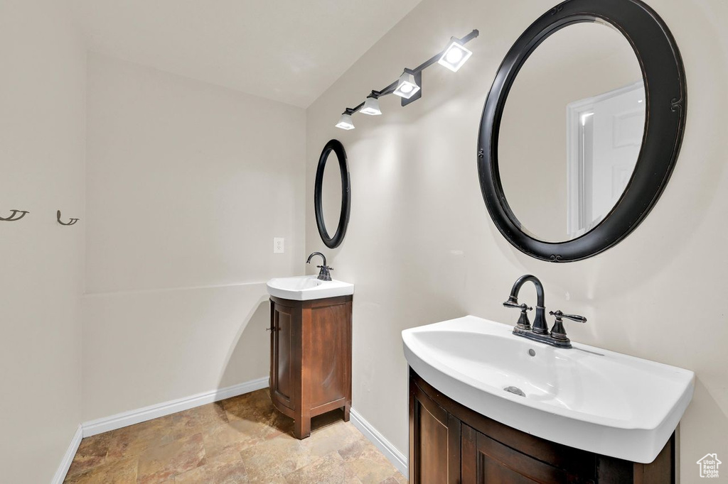 Bathroom with two vanities, baseboards, and stone finish flooring