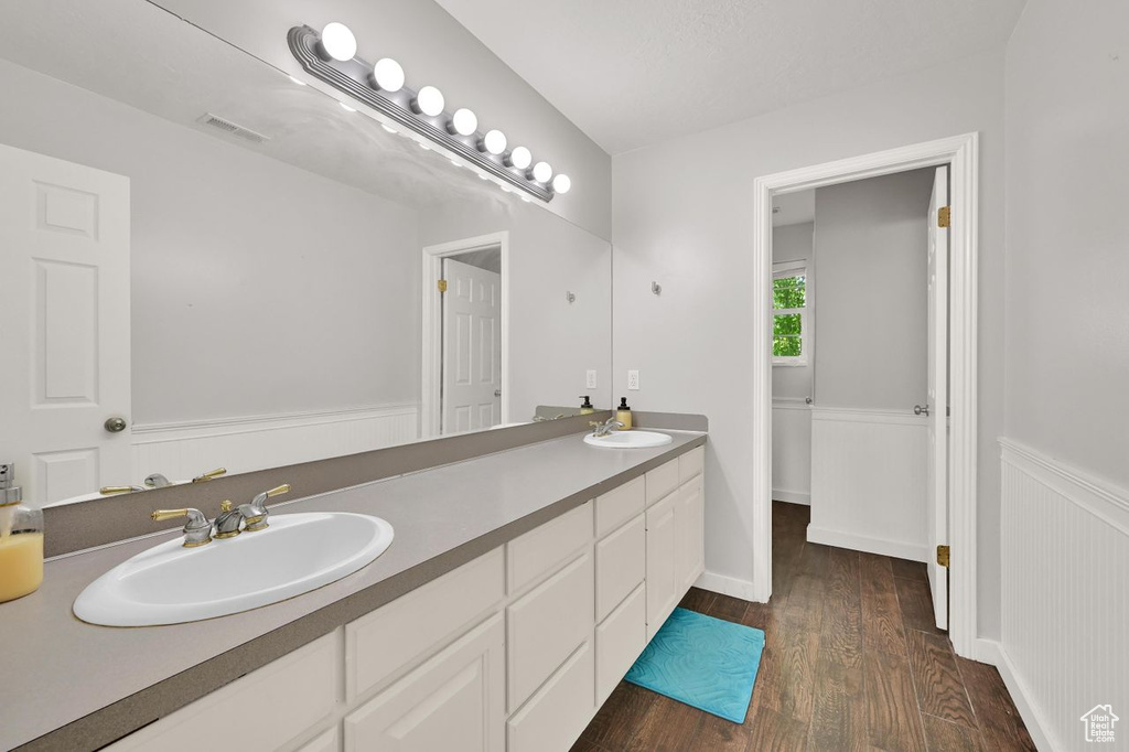 Bathroom with wood finished floors, double vanity, and a wainscoted wall