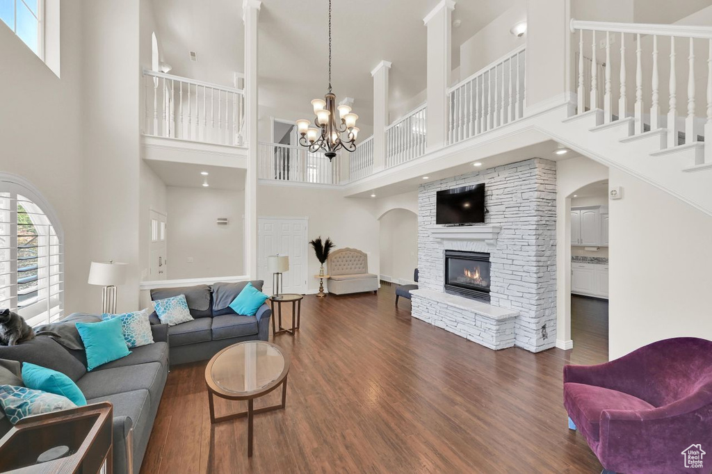 Living room featuring a towering ceiling, dark wood-type flooring, a fireplace, arched walkways, and a chandelier