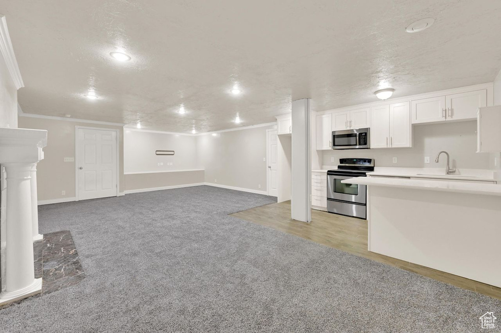 Kitchen with appliances with stainless steel finishes, light colored carpet, a sink, white cabinets, and light countertops