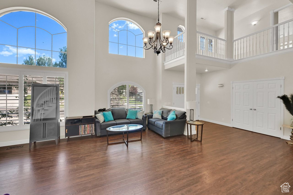 Living room with a high ceiling, dark wood-style flooring, a chandelier, and baseboards