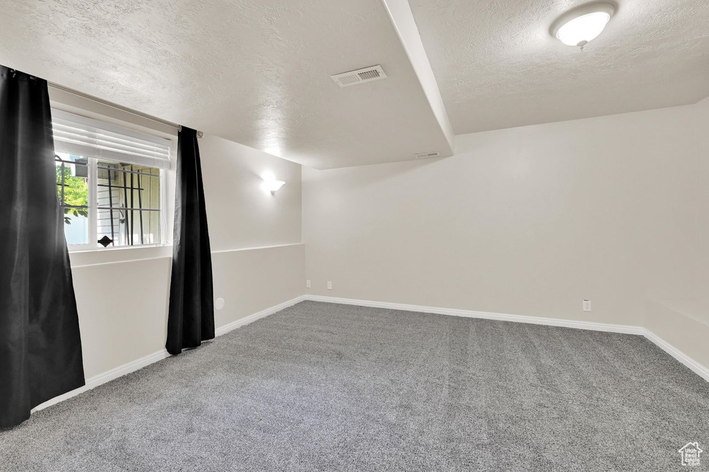 Carpeted empty room with a textured ceiling and baseboards