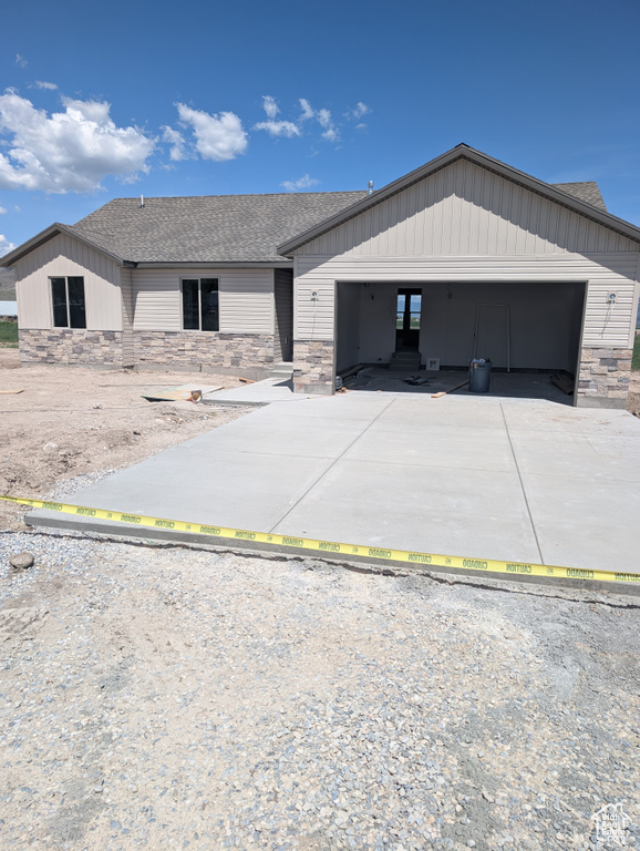View of front of house with stone siding, driveway, roof with shingles, and a garage