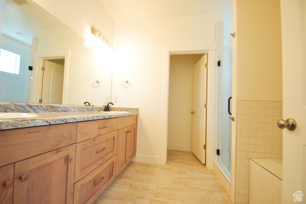 Full bathroom featuring a shower stall, double vanity, and baseboards