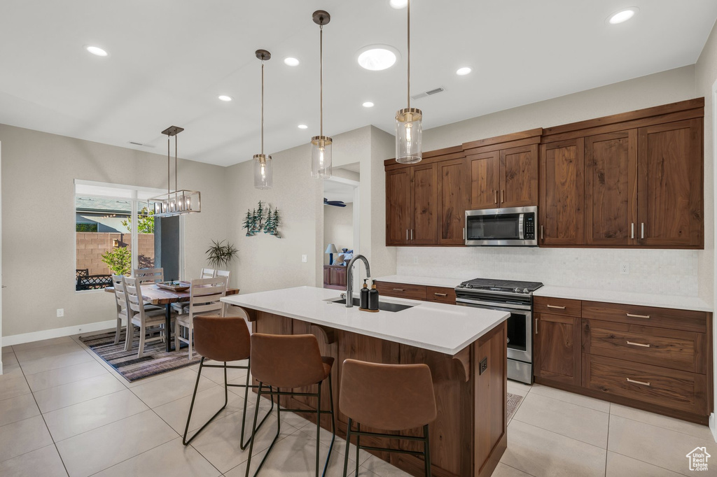 Kitchen with appliances with stainless steel finishes, a sink, light countertops, a breakfast bar, and an island with sink