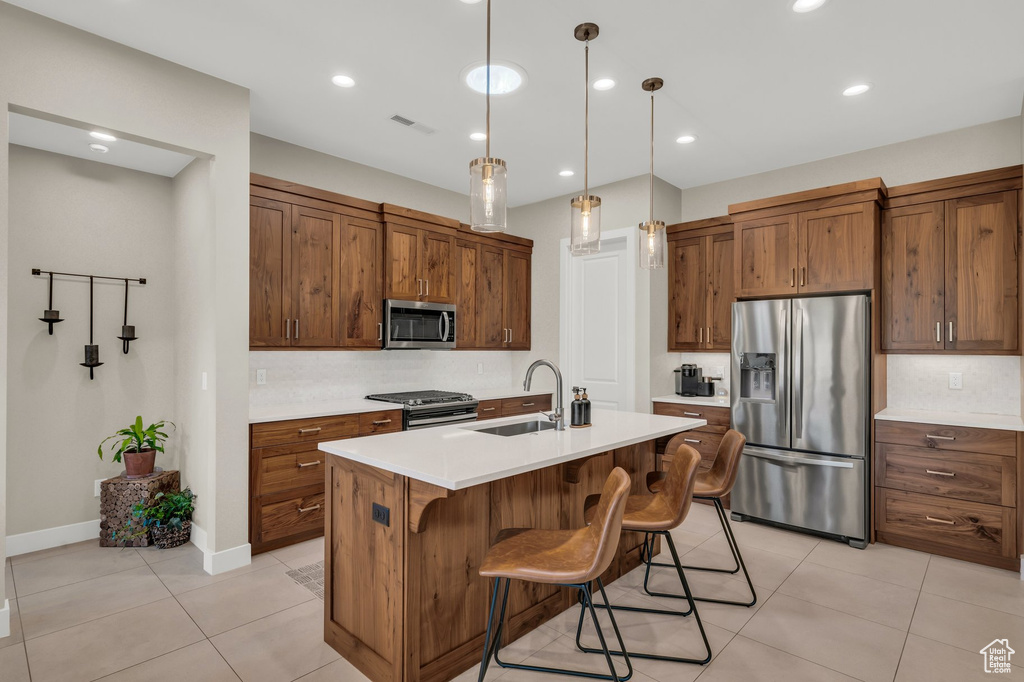 Kitchen with appliances with stainless steel finishes, a sink, light tile patterned flooring, light countertops, and a breakfast bar
