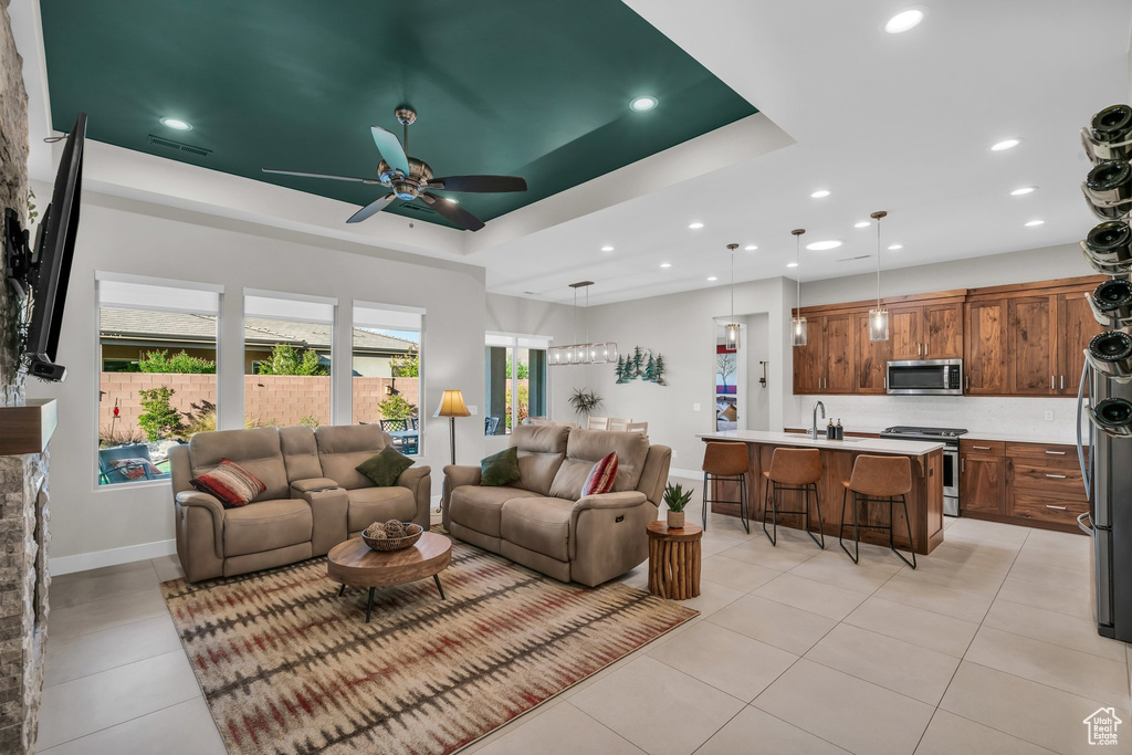 Living area featuring a tray ceiling, light tile patterned flooring, ceiling fan, recessed lighting, and baseboards