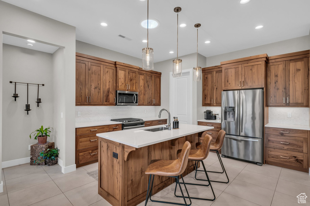 Kitchen featuring stainless steel appliances, a sink, light tile patterned flooring, brown cabinetry, and light countertops