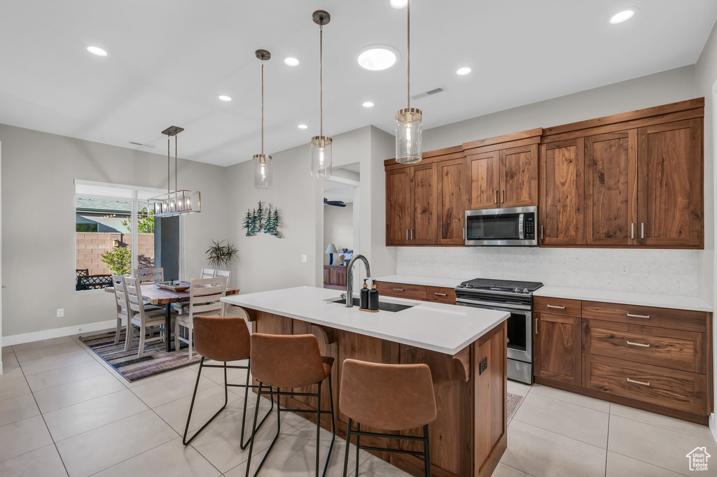 Kitchen featuring appliances with stainless steel finishes, a sink, light countertops, a breakfast bar area, and a kitchen island with sink