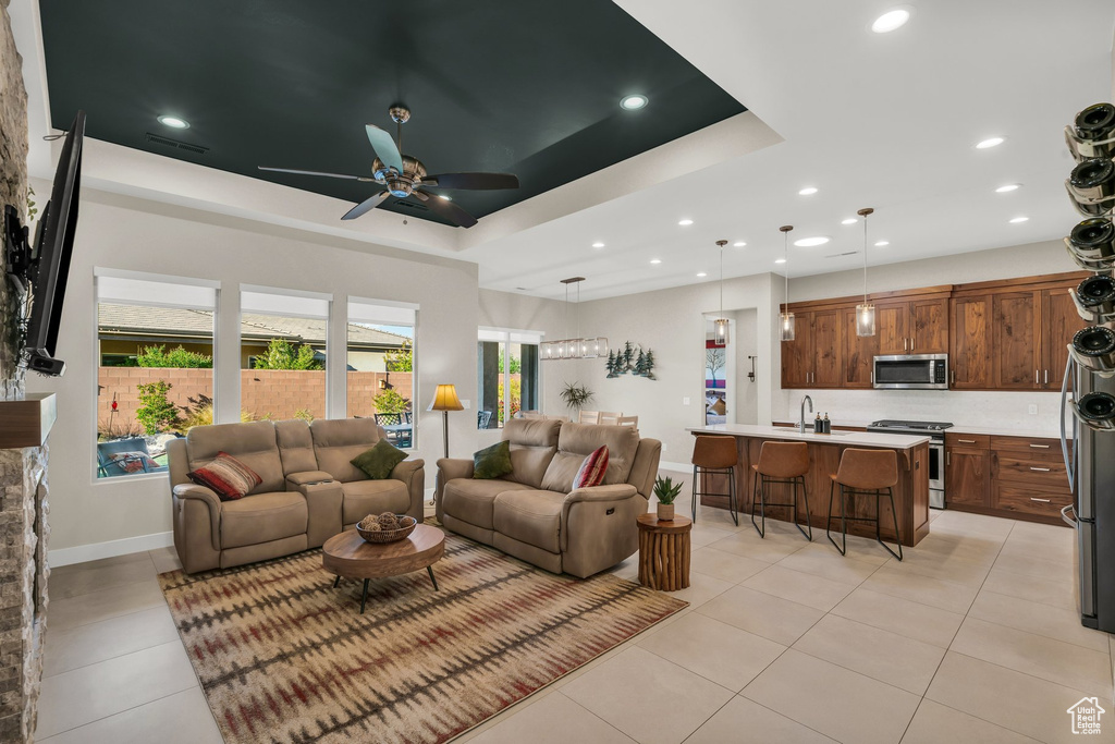 Living area featuring a ceiling fan, a tray ceiling, light tile patterned floors, recessed lighting, and baseboards